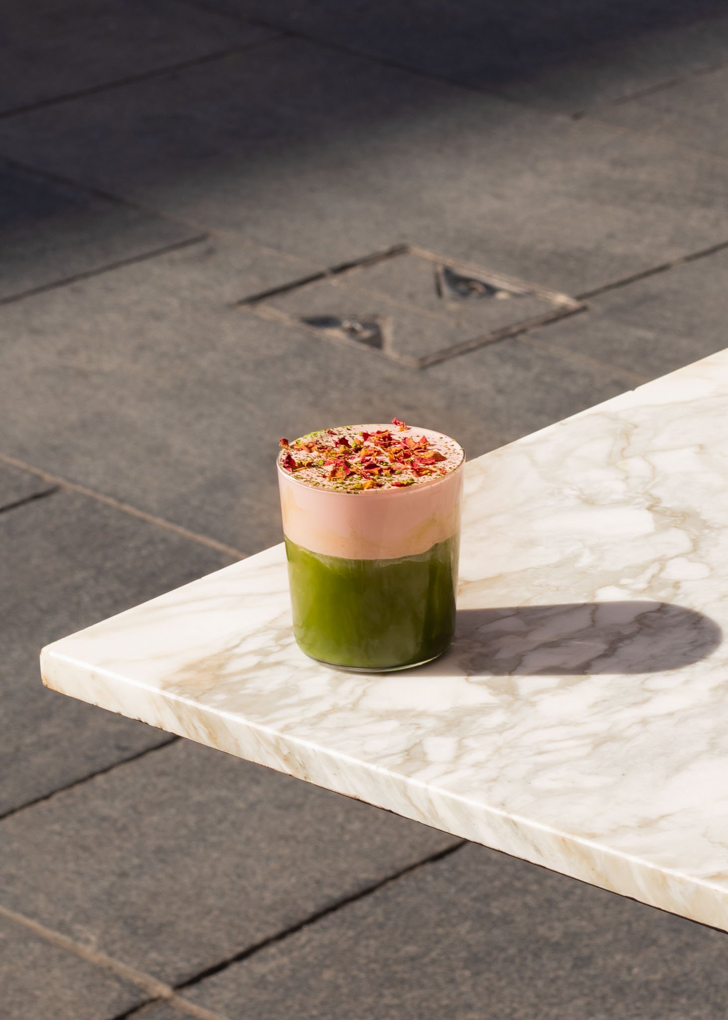 Layered green and pink drink with floral garnish on marble table