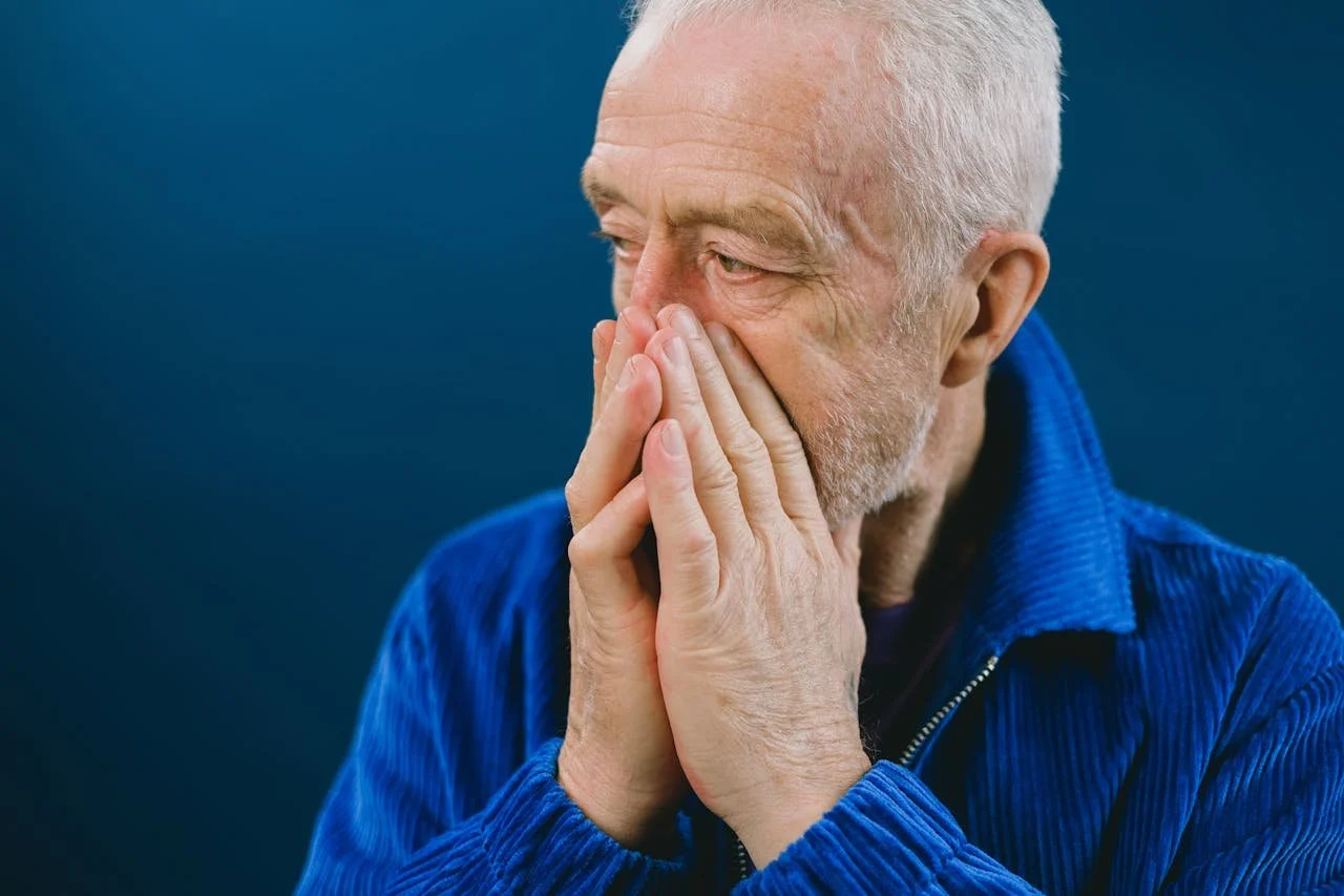 Elderly man holding his hands to his face