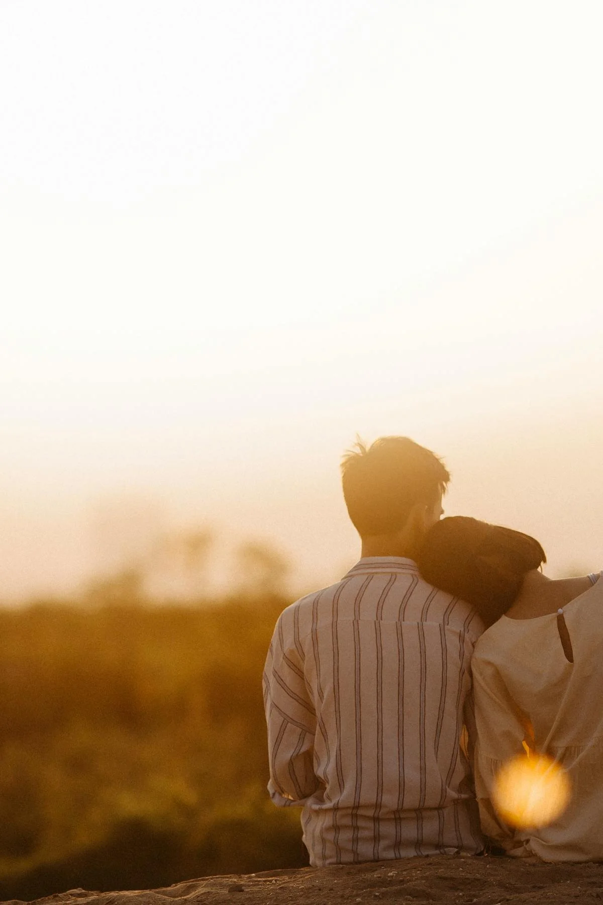 Man and woman sitting next to each other looking out into nature as woman rests her head on man's shoulders