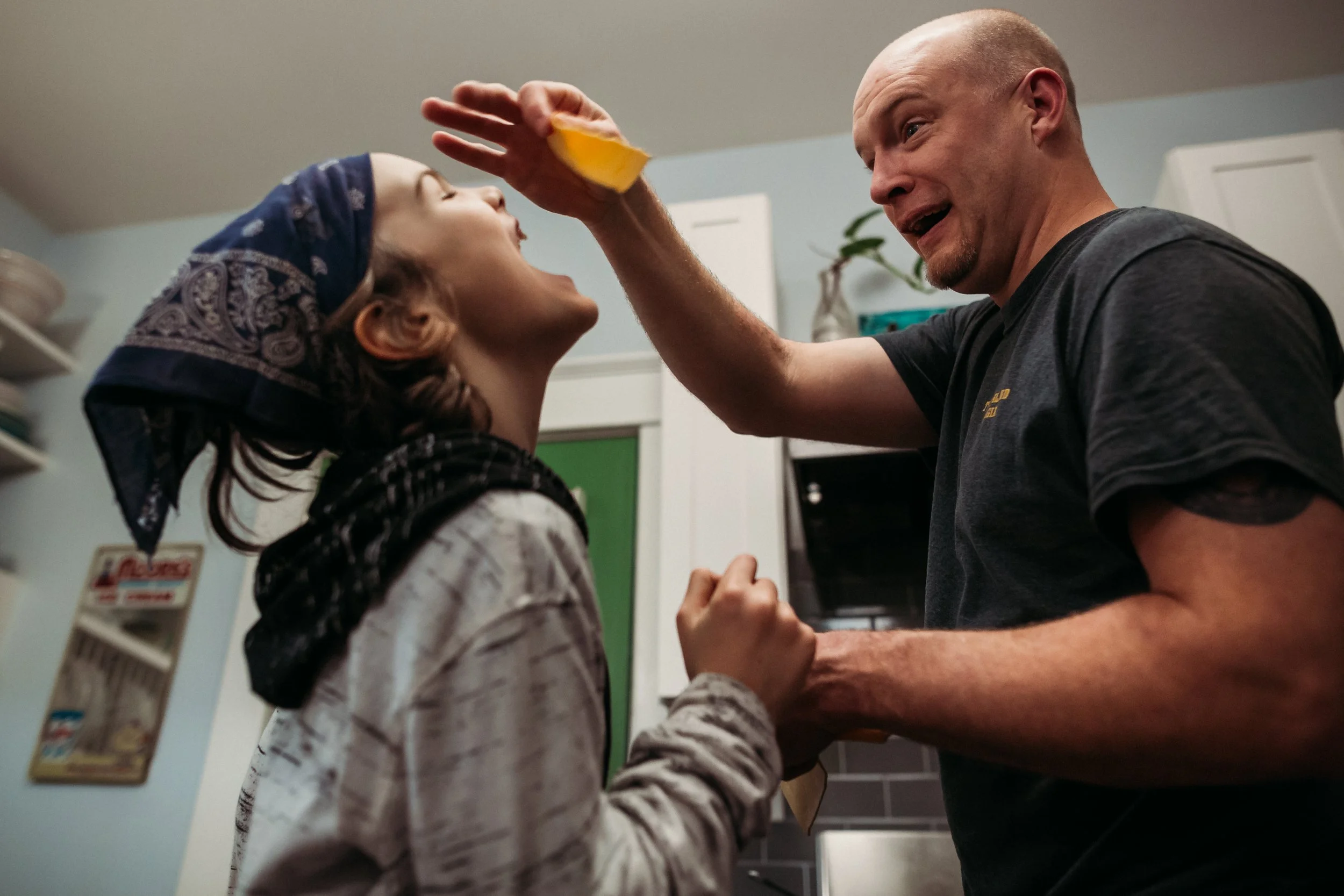 Father in the kitchen, holding a slice of cheese in the air for his laughing son
