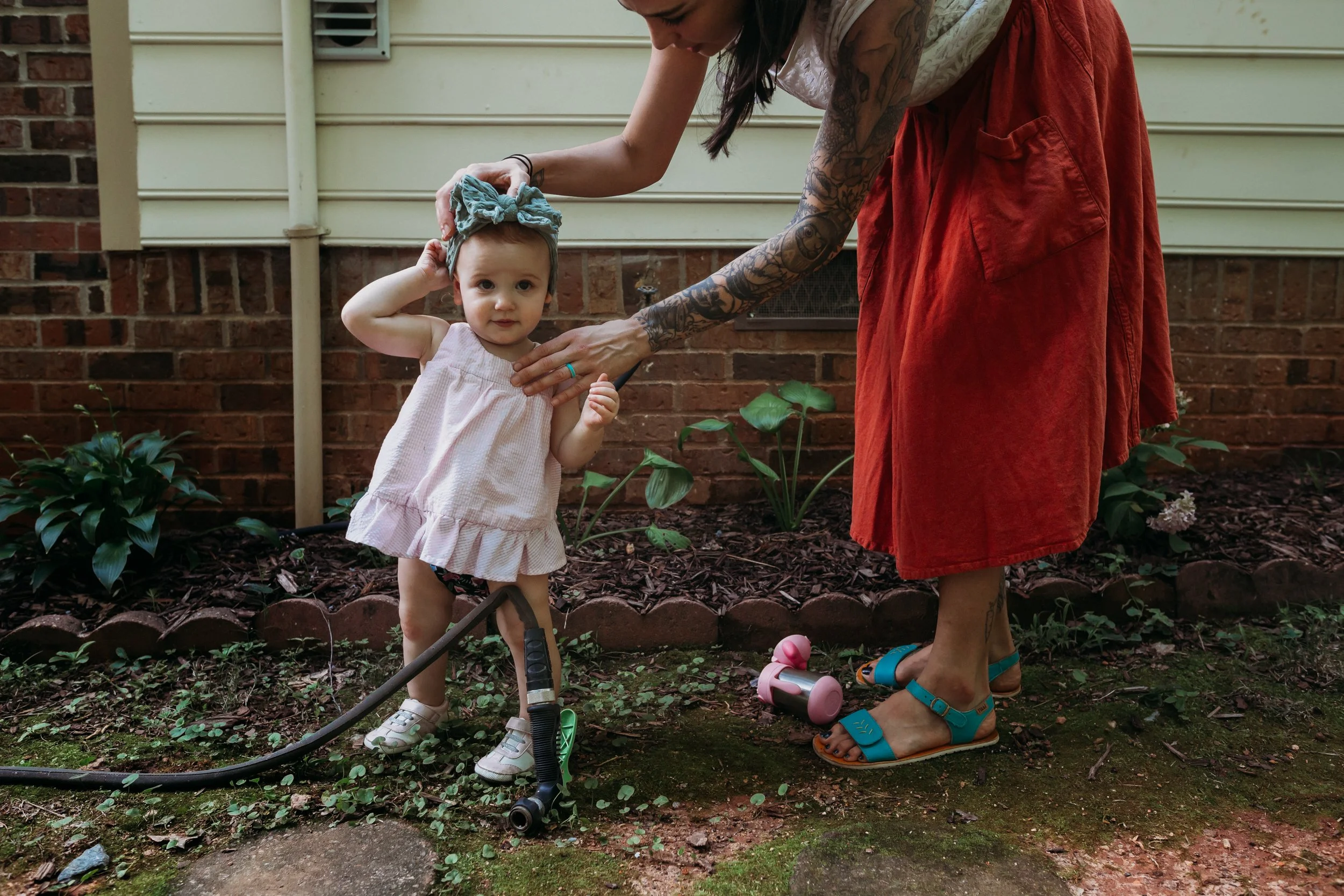 One year old girl standing next to her mom in their Atlanta yard