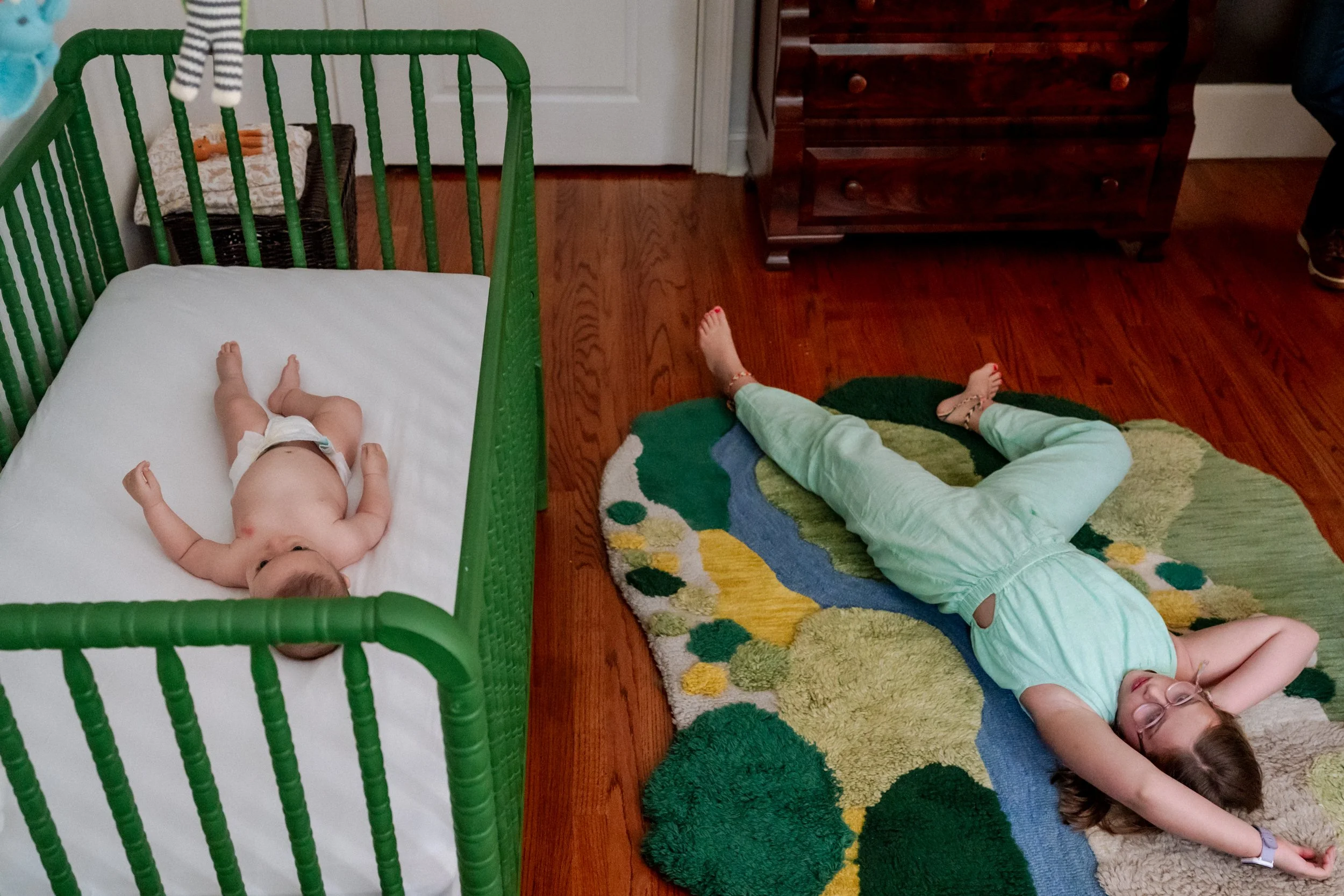 Newborn baby in the crib at home in Atlanta while big sister lies on the floor next to the crib