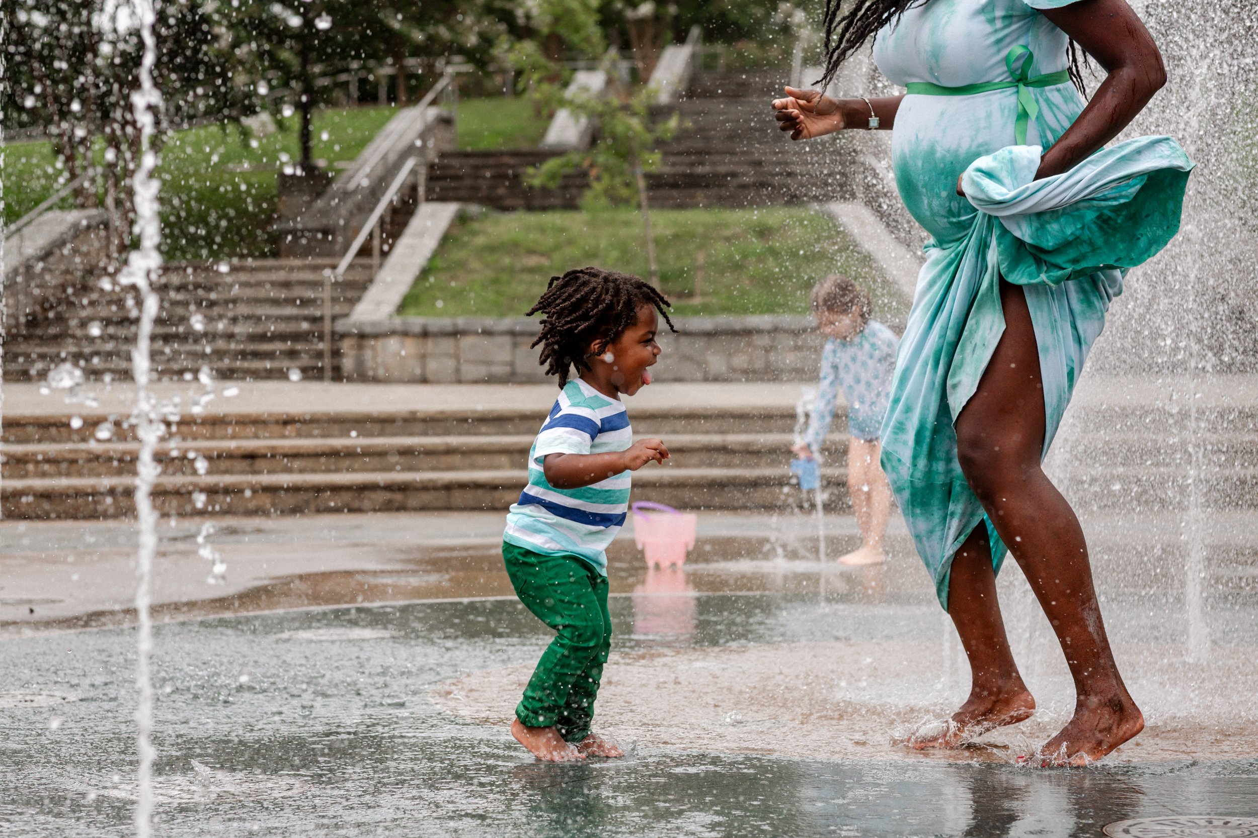LIttle boy jumping in the Old Fourth Ward splashpad in Atlanta with his pregnant mom