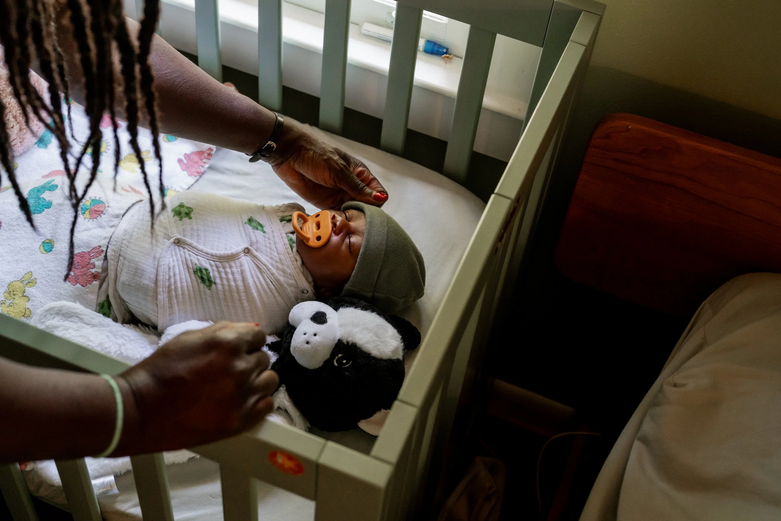 newborn baby asleep  in a crib while mom fixes his hat