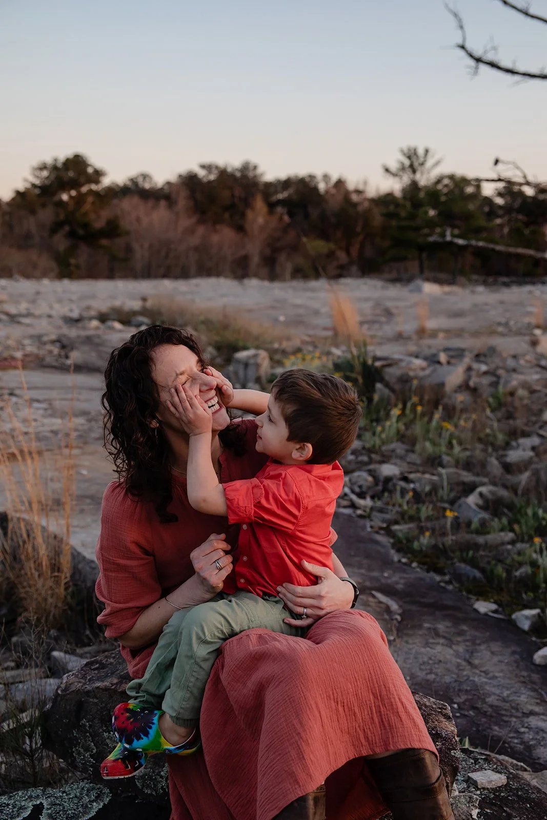 Little boy sitting on his moms lap, squeezing her face in his hands