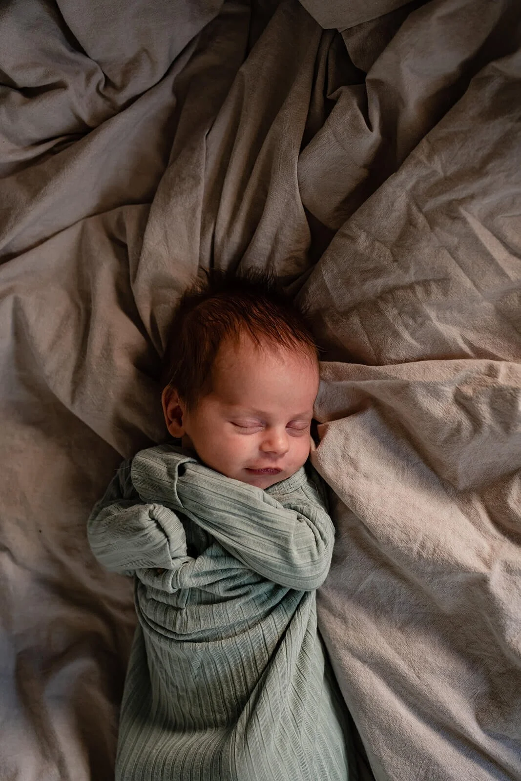 Newborn baby asleep on a bed at home in a green jumper