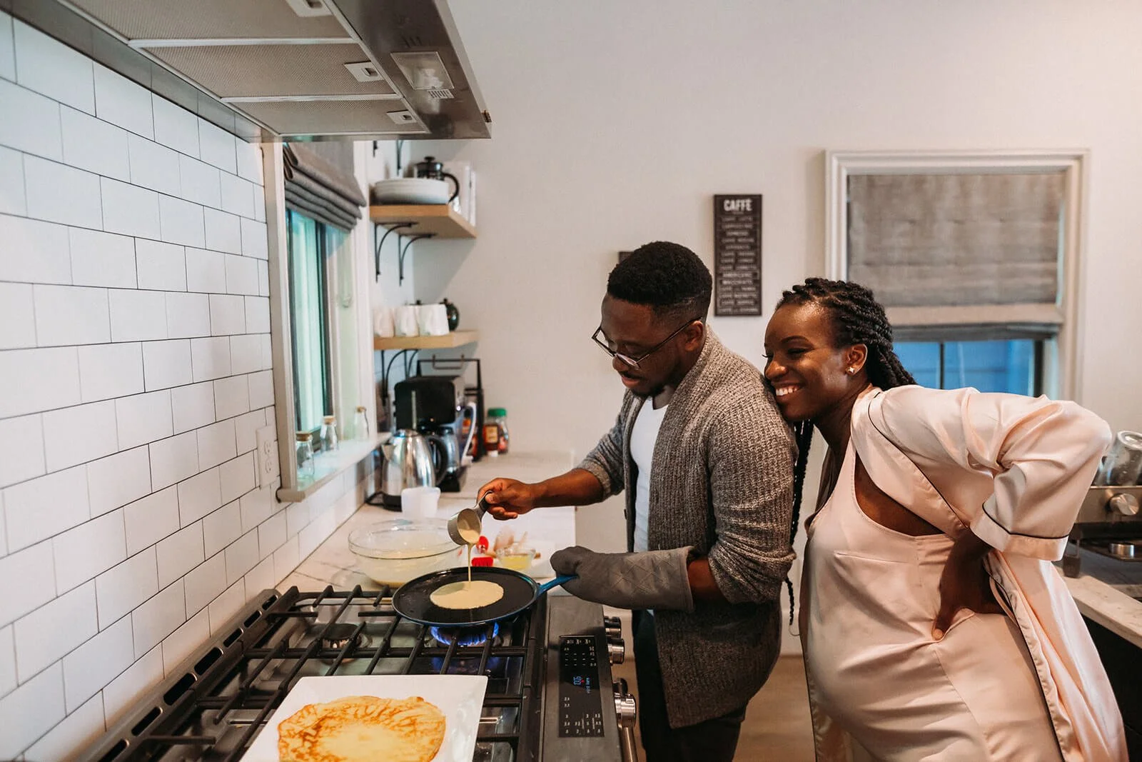 pregnant mom leaning on her husband as he makes breakfast at home in Atlanta