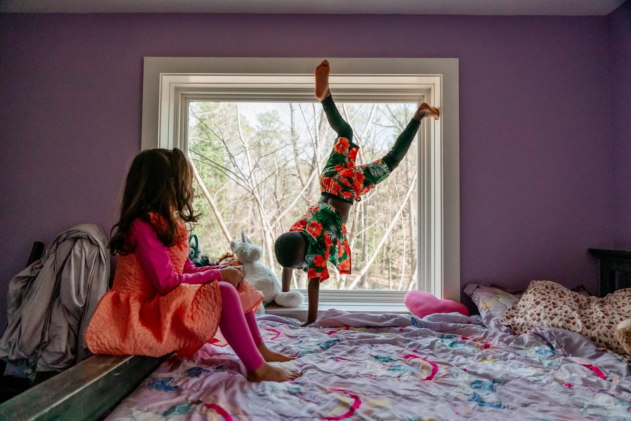 Young boy doing a handstand on the bed at home while his sister watches