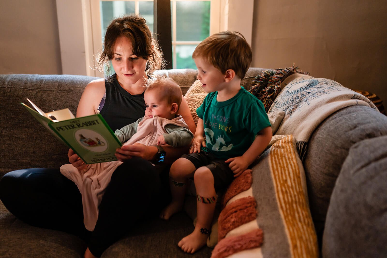 mom reading a story to her baby and toddler on the couch at home