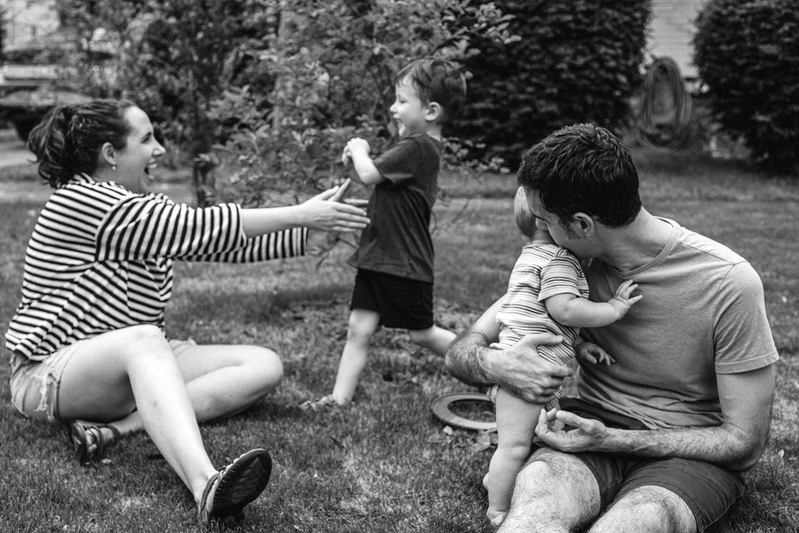 Family sitting in their yard, the little boy running into his moms arms