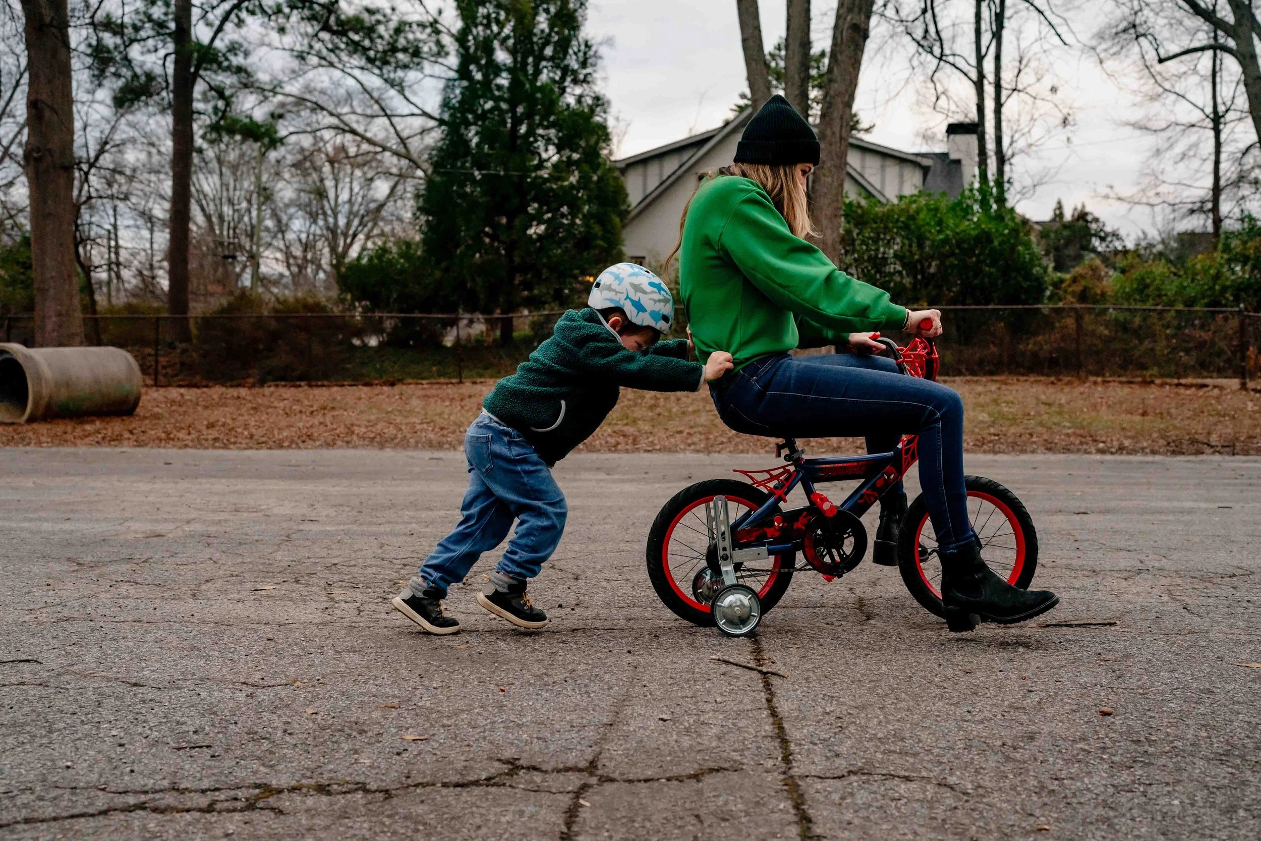 Little boy wearing a bike helmet and pushing his mom on his tiny bike at a Decatur park