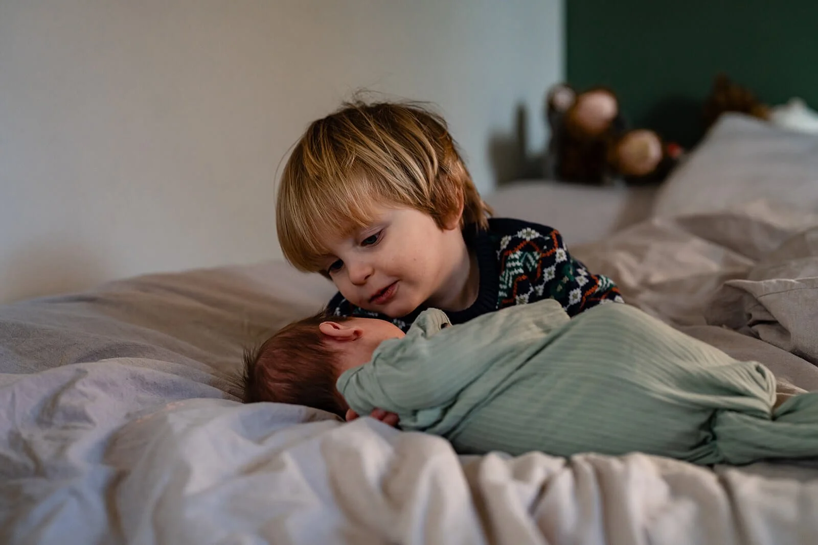 young boy looking at his newborn baby sister on the bed at home