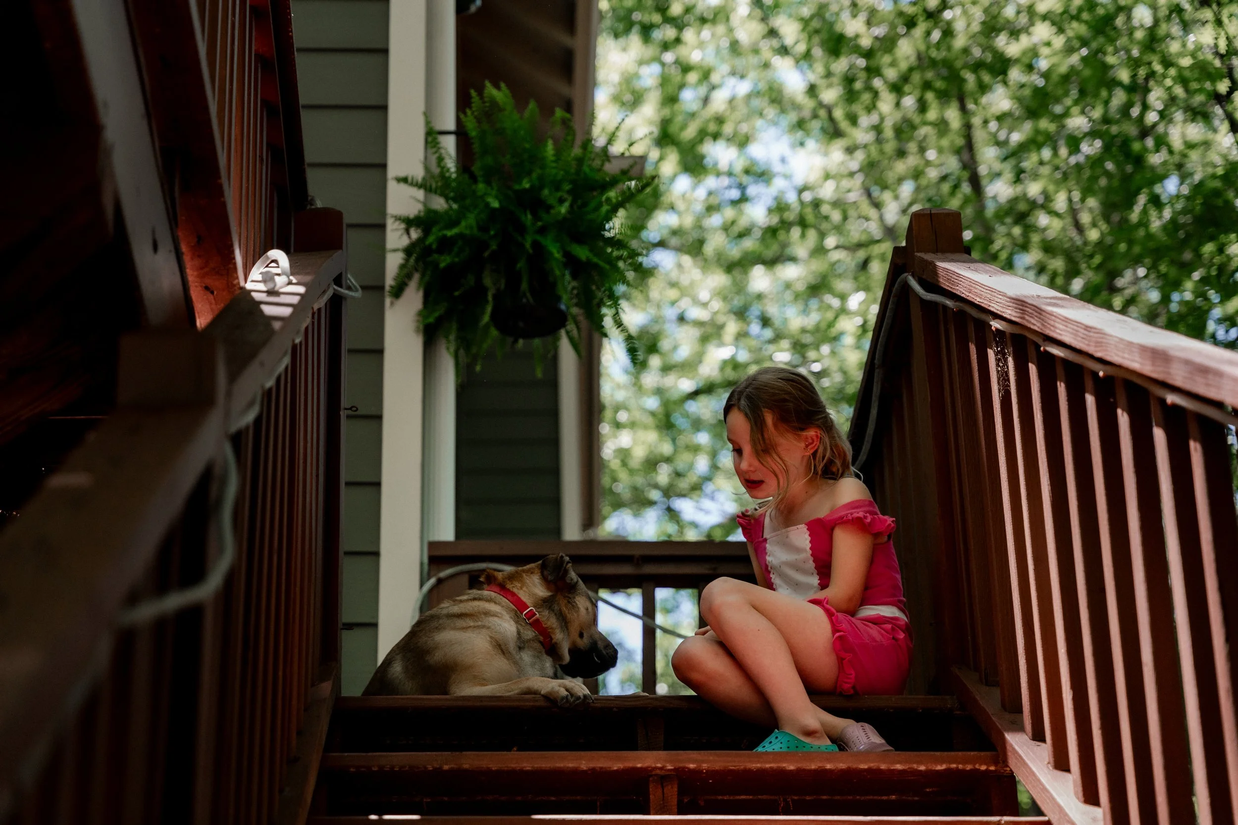 Young girl sitting on the steps of her home with her dog