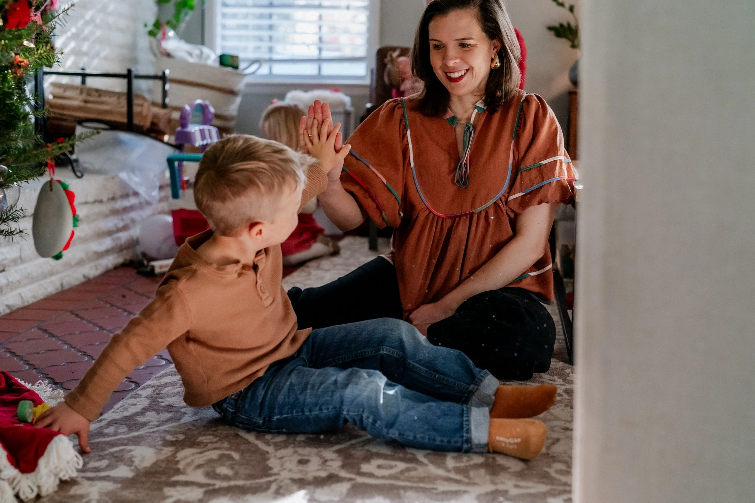 Mom sitting on the living room floor high fiving her son