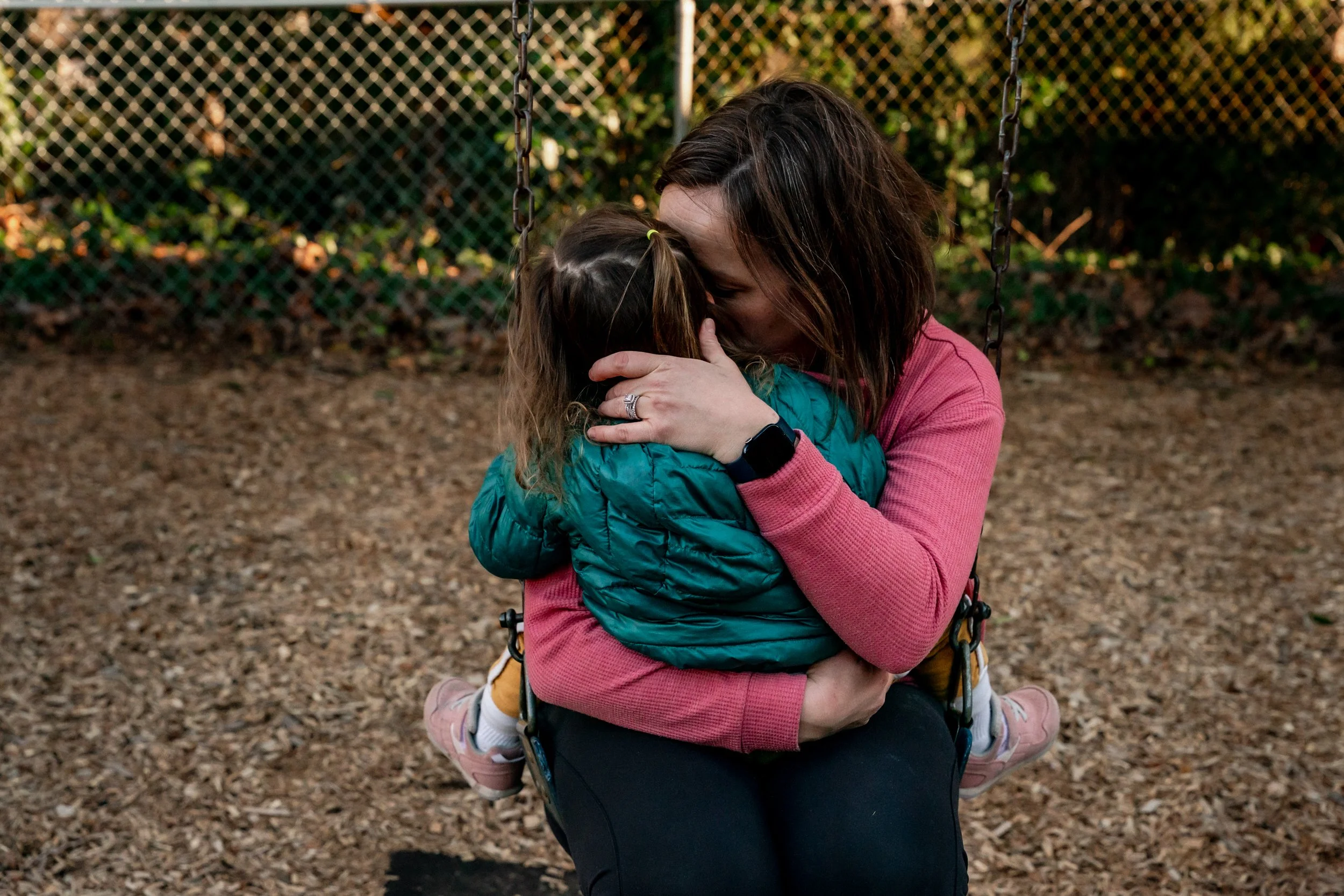 Mom holding her daughter in a snuggle on the swing at a playground