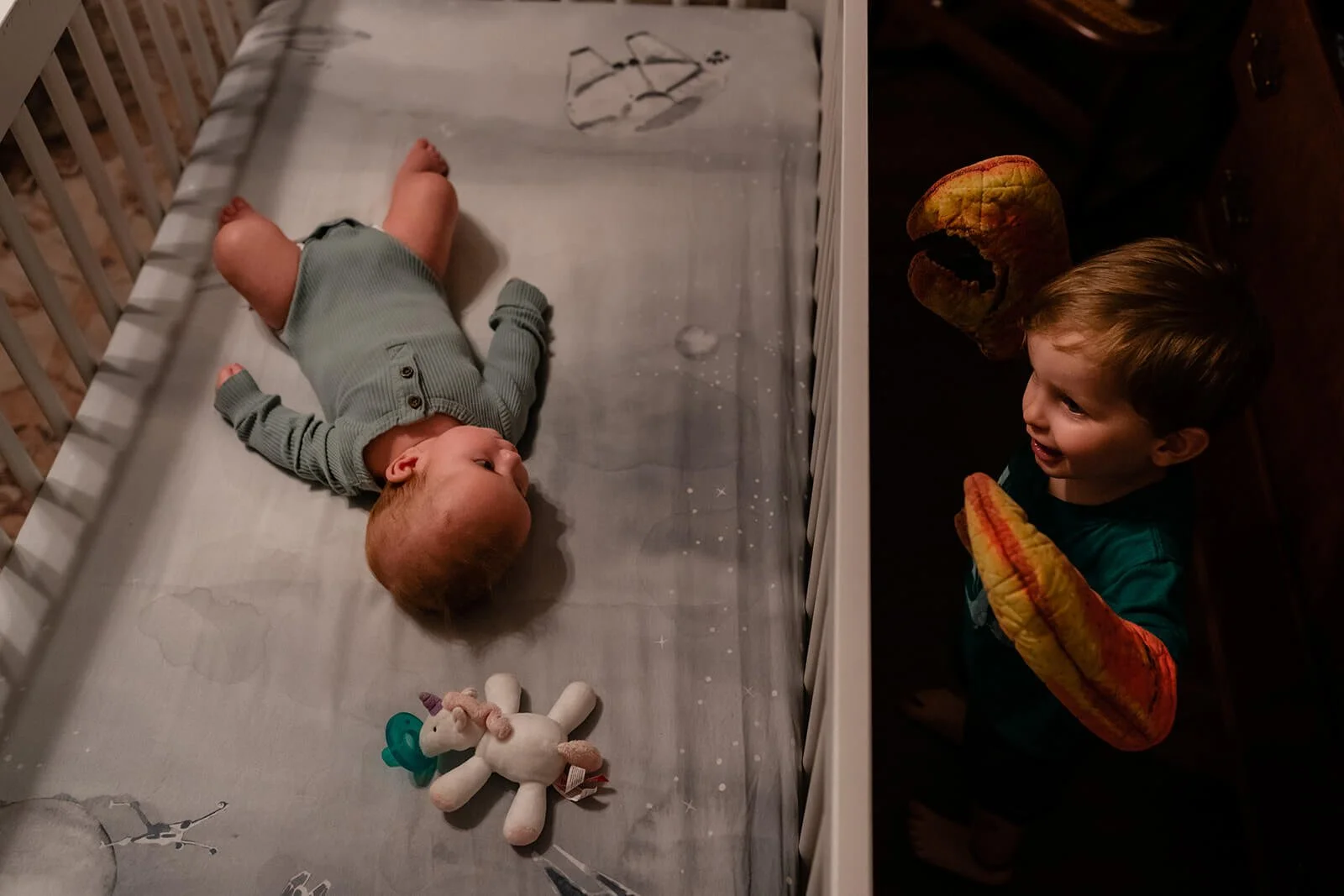 big brother looking in the crib at his baby sister