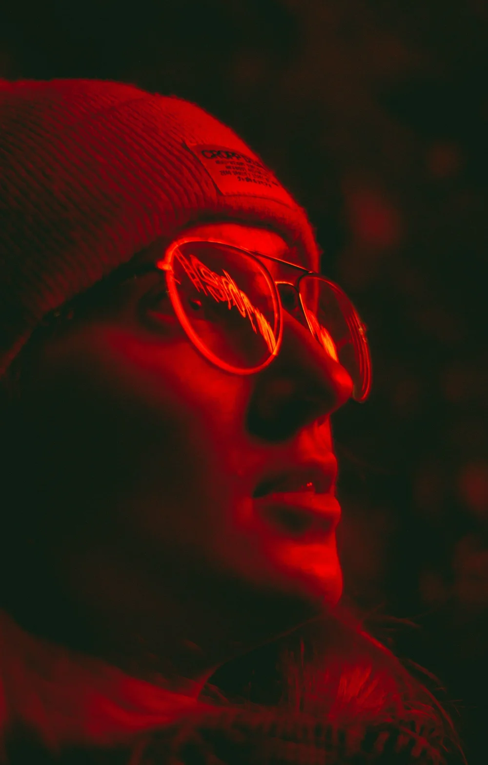 A face lit in red light, wearing glasses