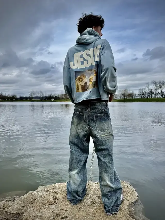 Customer wearing the Baptized hoodie by a lake, back with the printed design