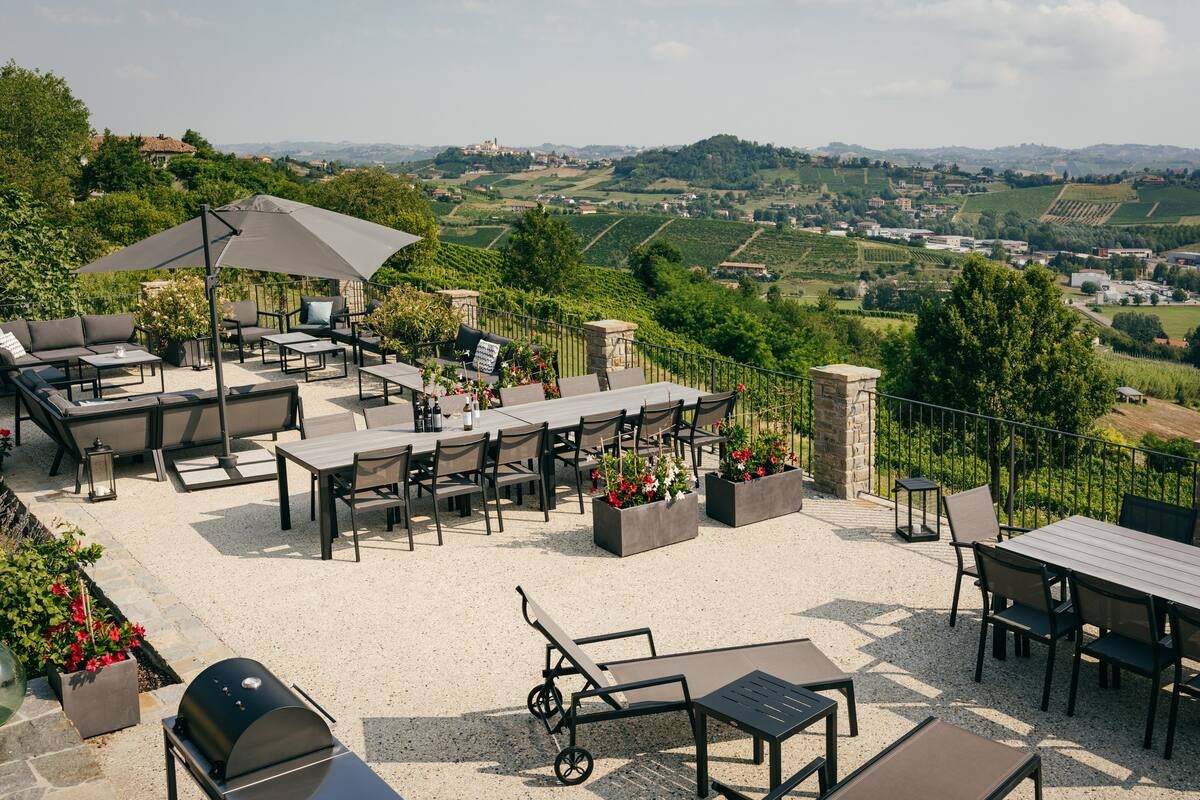 Outdoor patio with tables, chairs, umbrellas, and lounge chairs overlooking vineyards and countryside landscape.