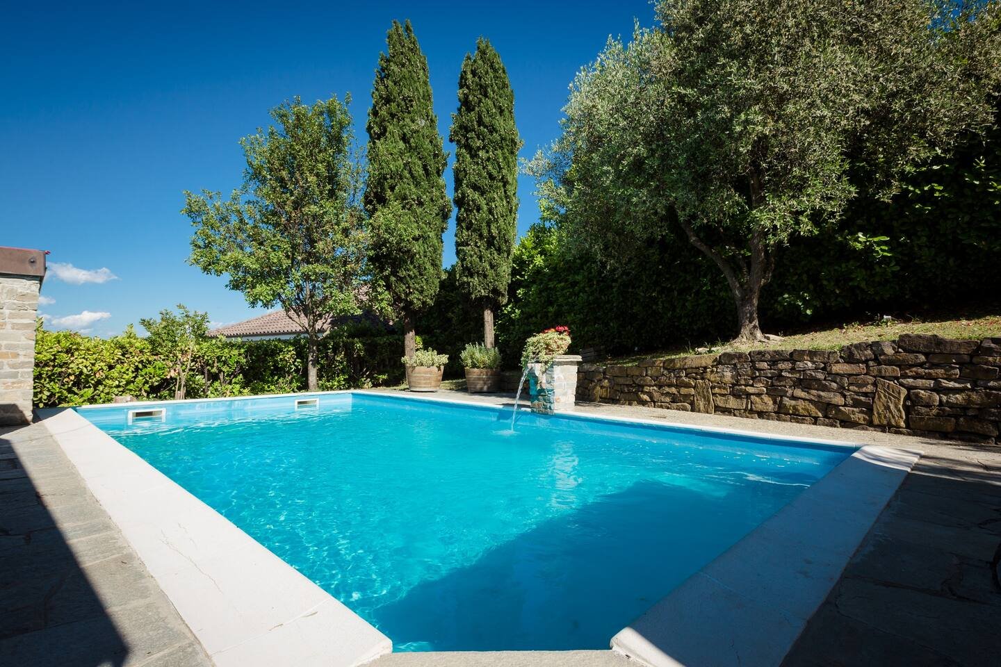 Outdoor swimming pool surrounded by trees and stone walls on a sunny day.