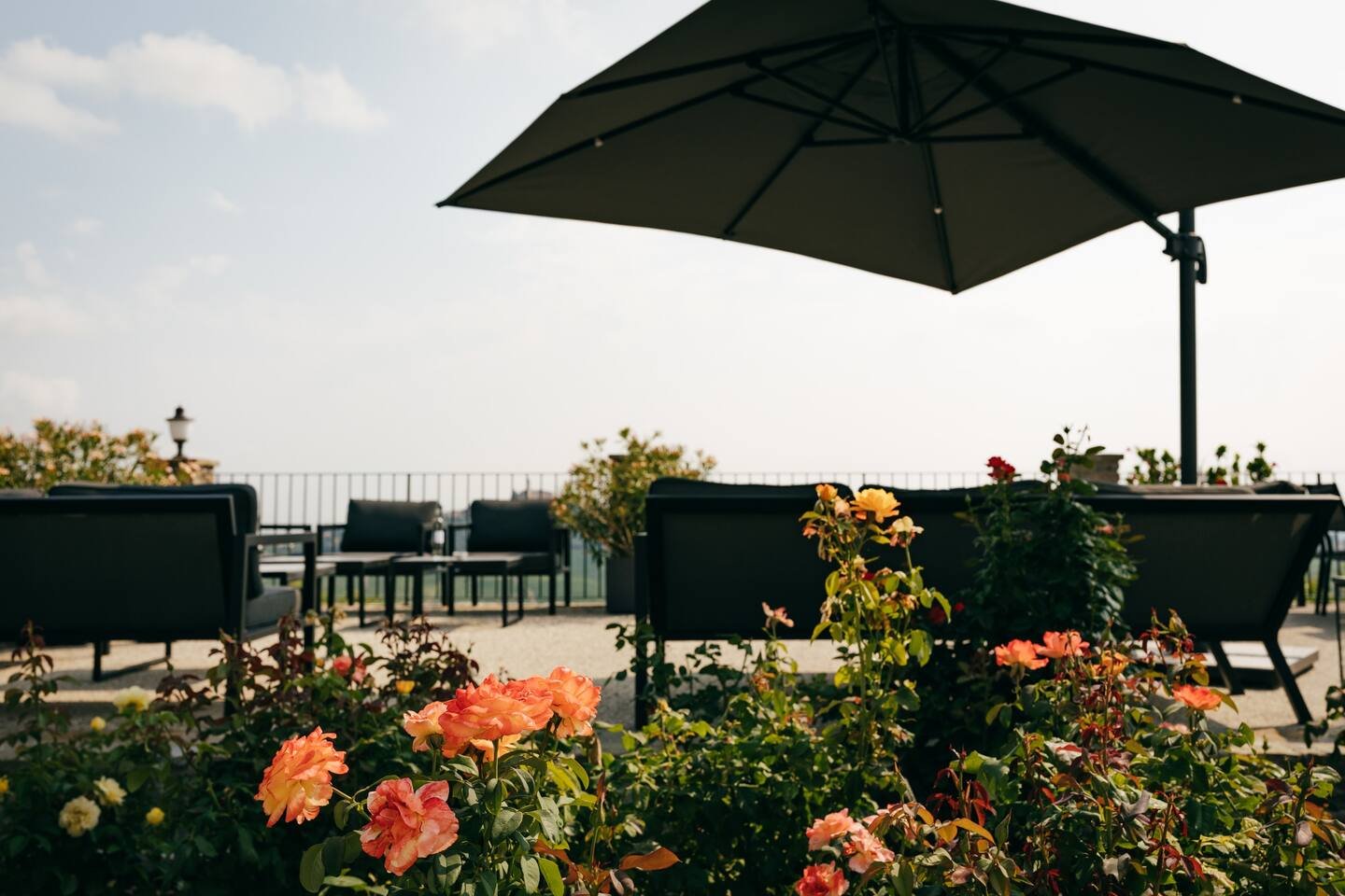 Outdoor patio area with black furniture and colorful flowers, including roses, under a large umbrella.