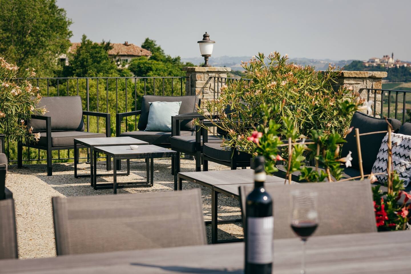 Outdoor patio with seating, tables, plants, wine bottle, and glass, overlooking countryside.
