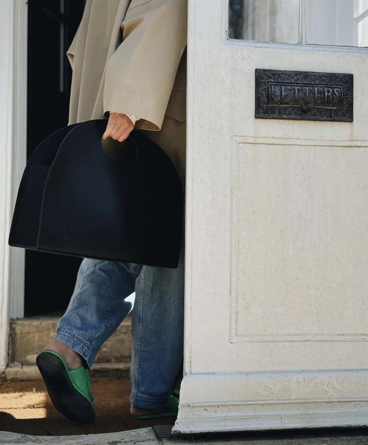 Large statement tote bag with cut out handle being held by a white front door
