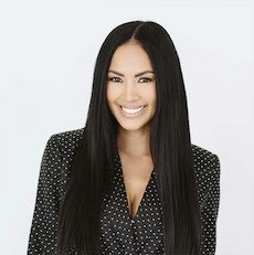 Rachel Taravella A woman with long black hair, smiling, wearing a black and white polka dot blazer against a plain white background.