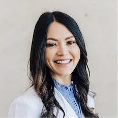Dr. Suzy Kingston Portrait of a smiling woman with dark hair and a white shirt, against a neutral background.