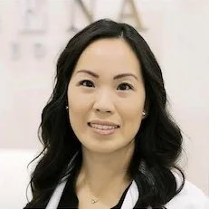 Karen Leong A woman with long black hair, wearing a white jacket, smiling inside a bright, modern office.