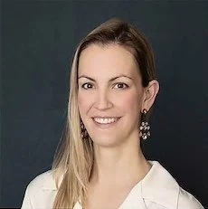 Claire Melancon - A woman with long blonde hair smiling, wearing earrings and a white top, against a dark background.