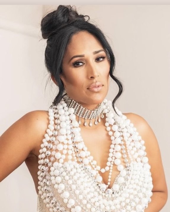 Rupa Jolly Woman wearing a white pearl necklace and choker, with dark hair styled in a bun, posing indoors.