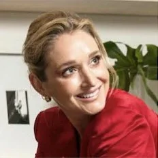 Paige Goss - A woman with blonde hair smiling, wearing a red top, in an indoor setting.