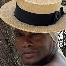 Parrish Lee
Milliner Close-up of a man wearing a straw hat with a black ribbon, outdoors near a tree.
