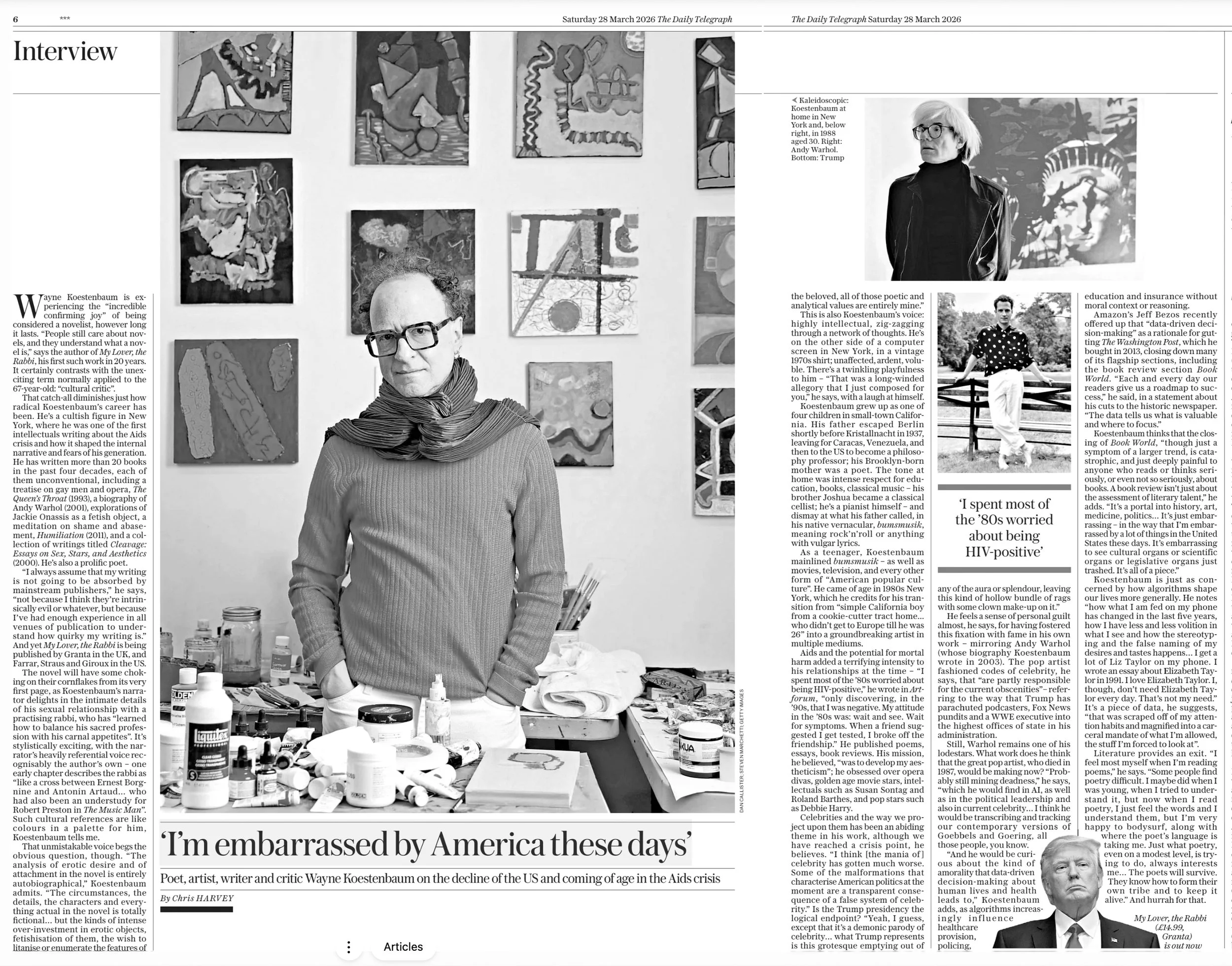 Black and white photograph of an art gallery wall with multiple abstract paintings. In front of the wall is a woman with glasses, short hair, and a scarf, sitting at a table with art supplies and bottles. The image appears to be part of a newspaper a