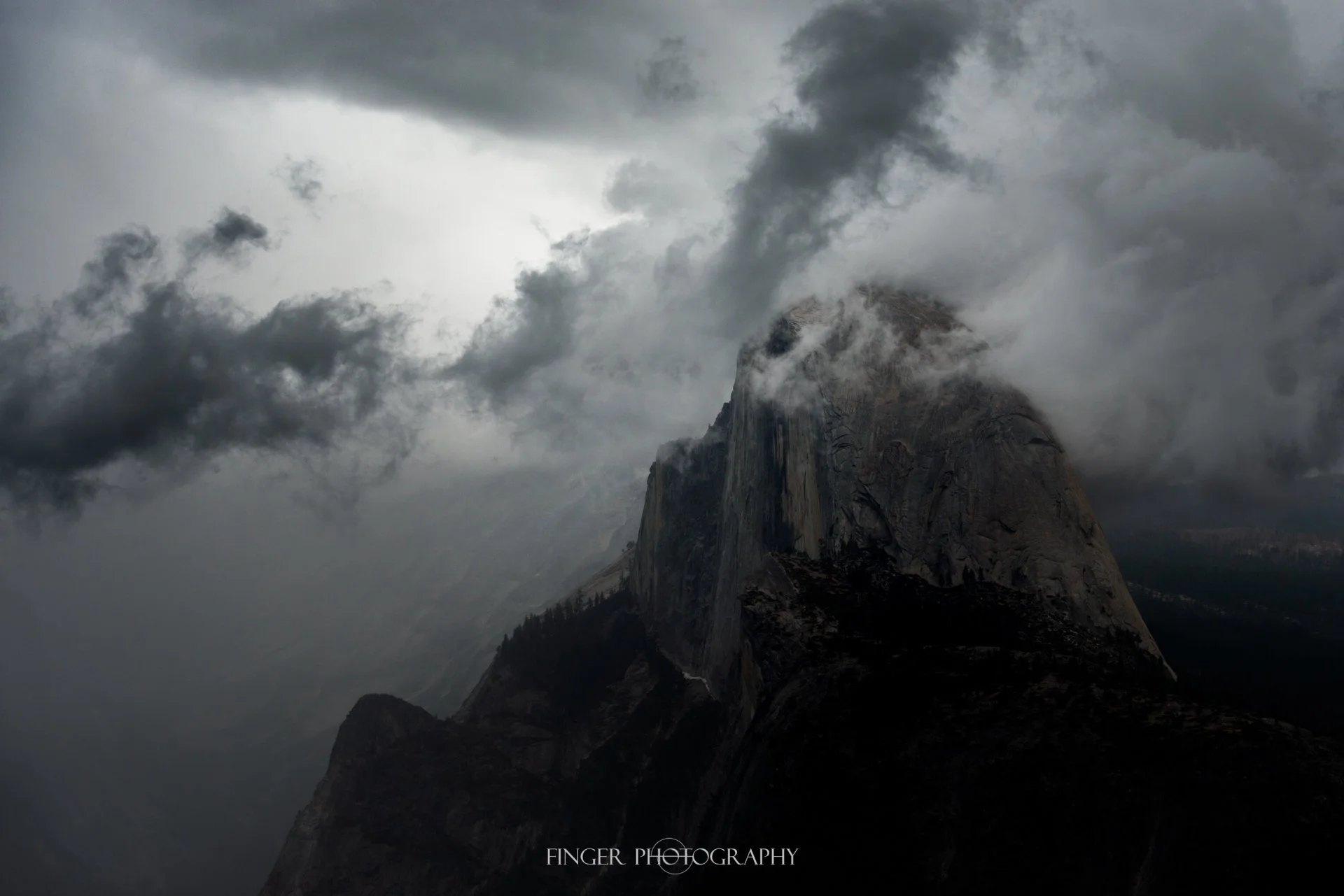 A Dramatic shot of Half Dome poking into some storm clouds.