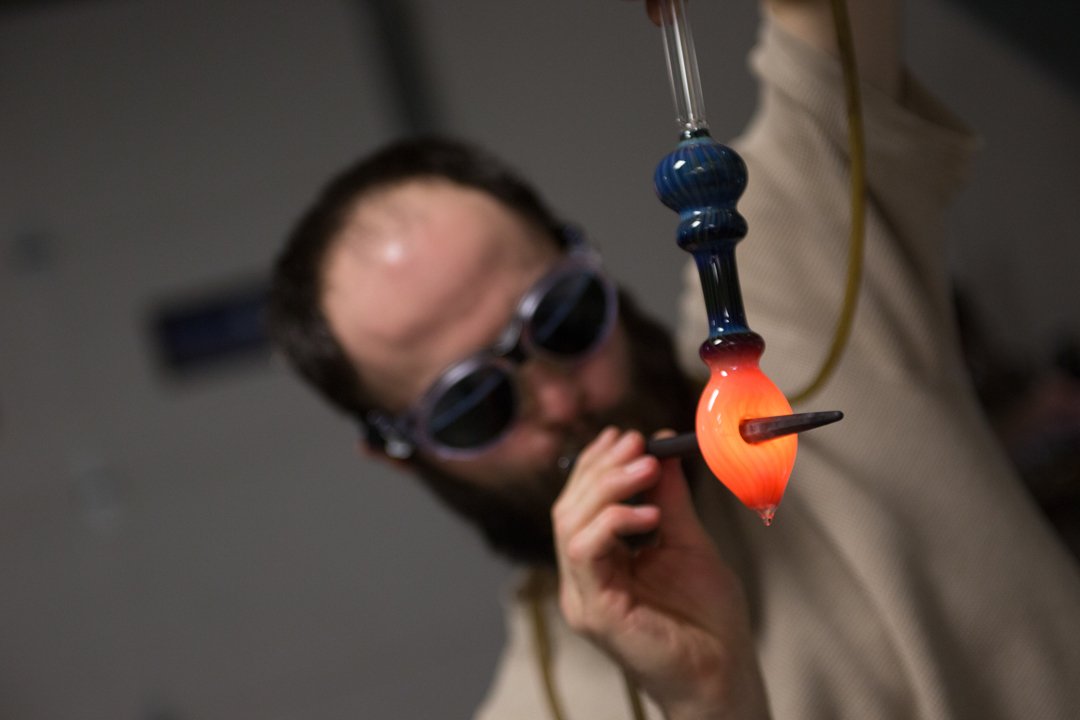 glass blower poking hole through warm part of pipe, shot by commercial photographer Corey Rourke

