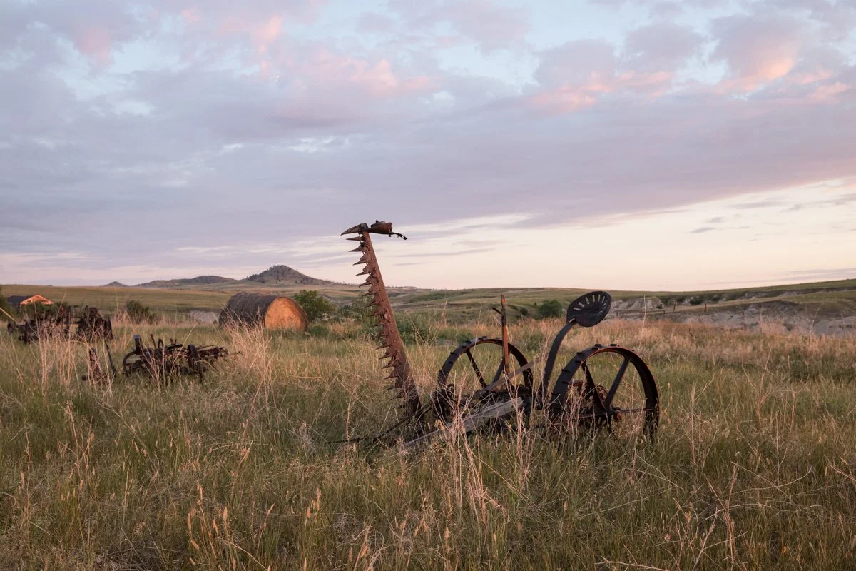 rusty farm equipment in a field with the morning sunrise
