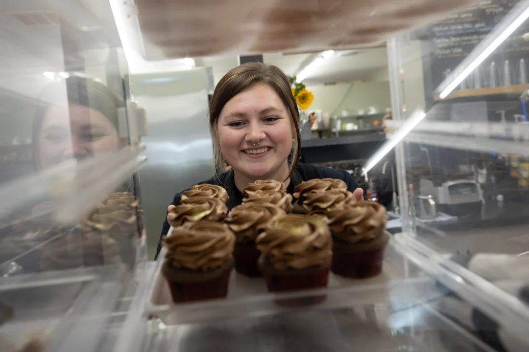 woman putting cupcakes into a case, shot by commercial photographer Corey Rourke

