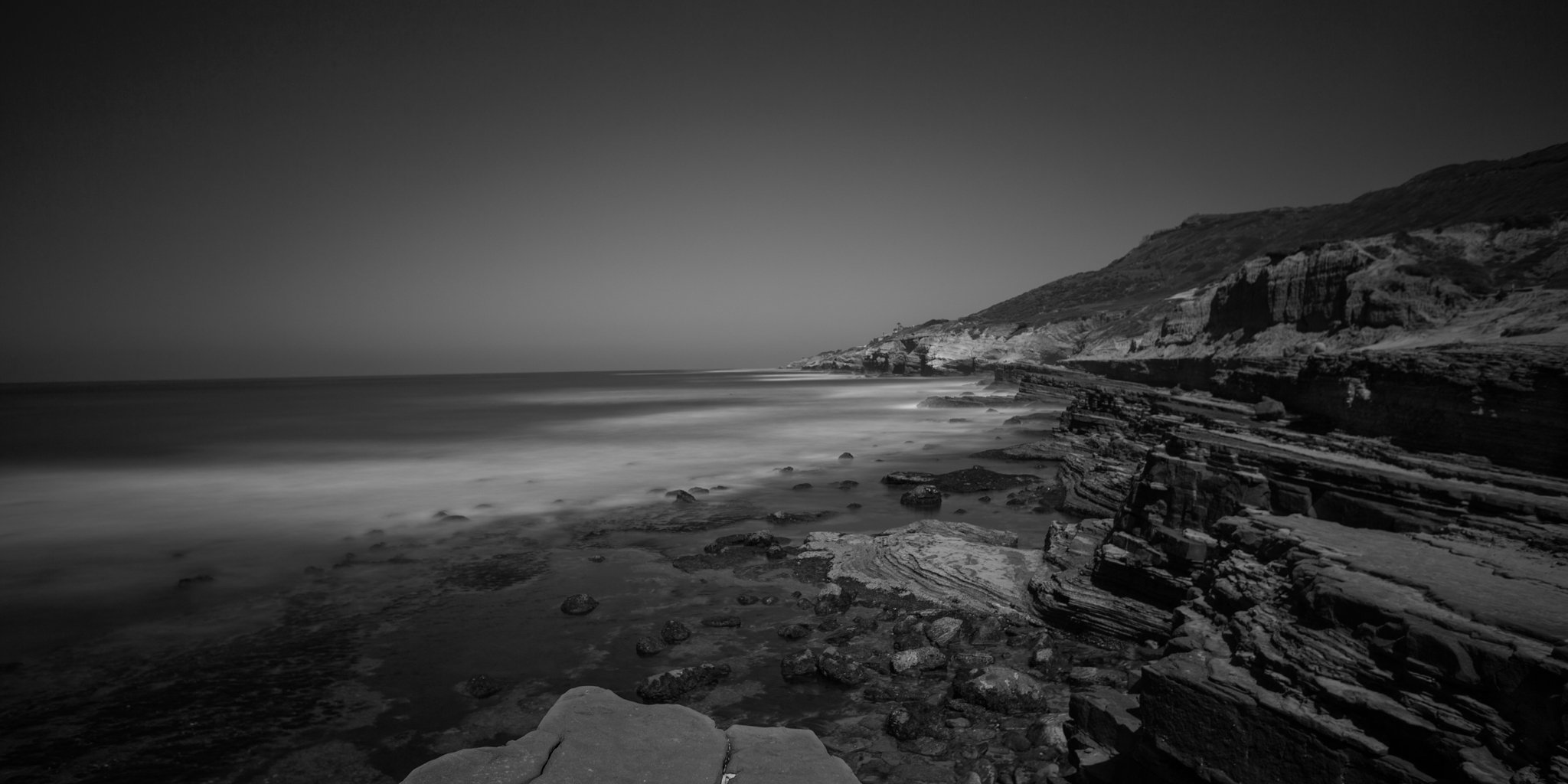 black and white moody image of San Diego coast with rocks in the foreground and ocean in the distance
