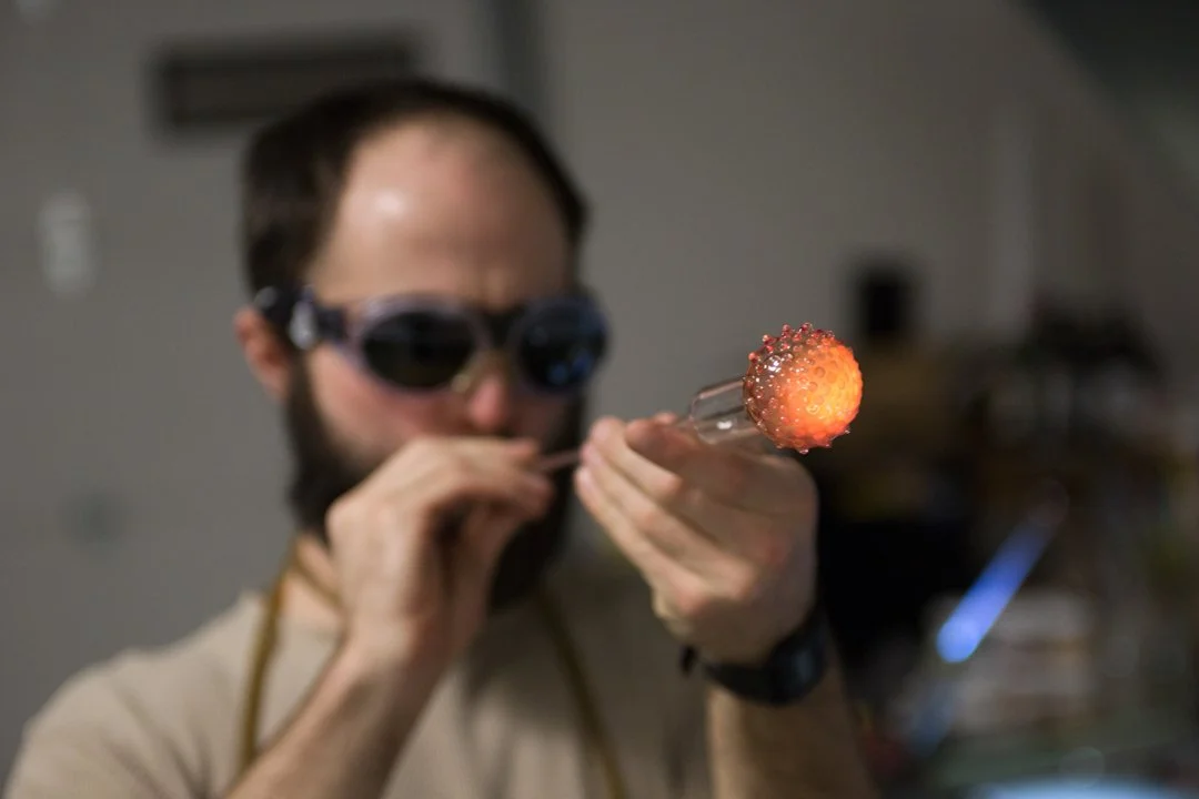 glass blower blowing air into hot yellow glass making the end larger, shot by commercial photographer Corey Rourke
 