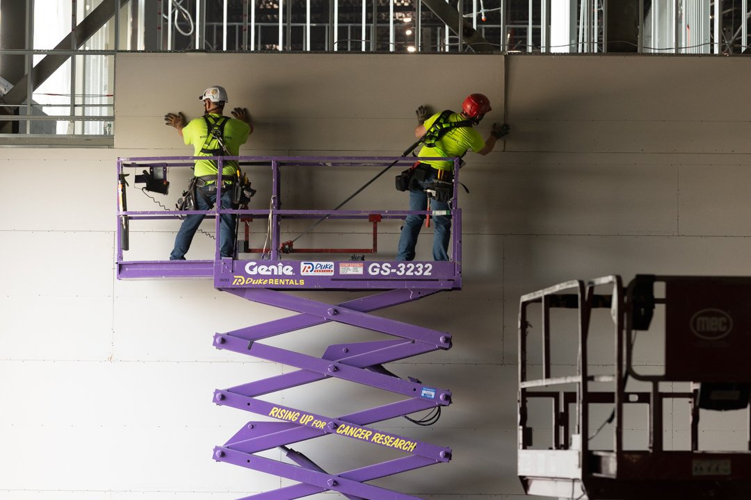 two construction workers on a lift placing siding on wall. shot by commercial photographer Corey Rourke
