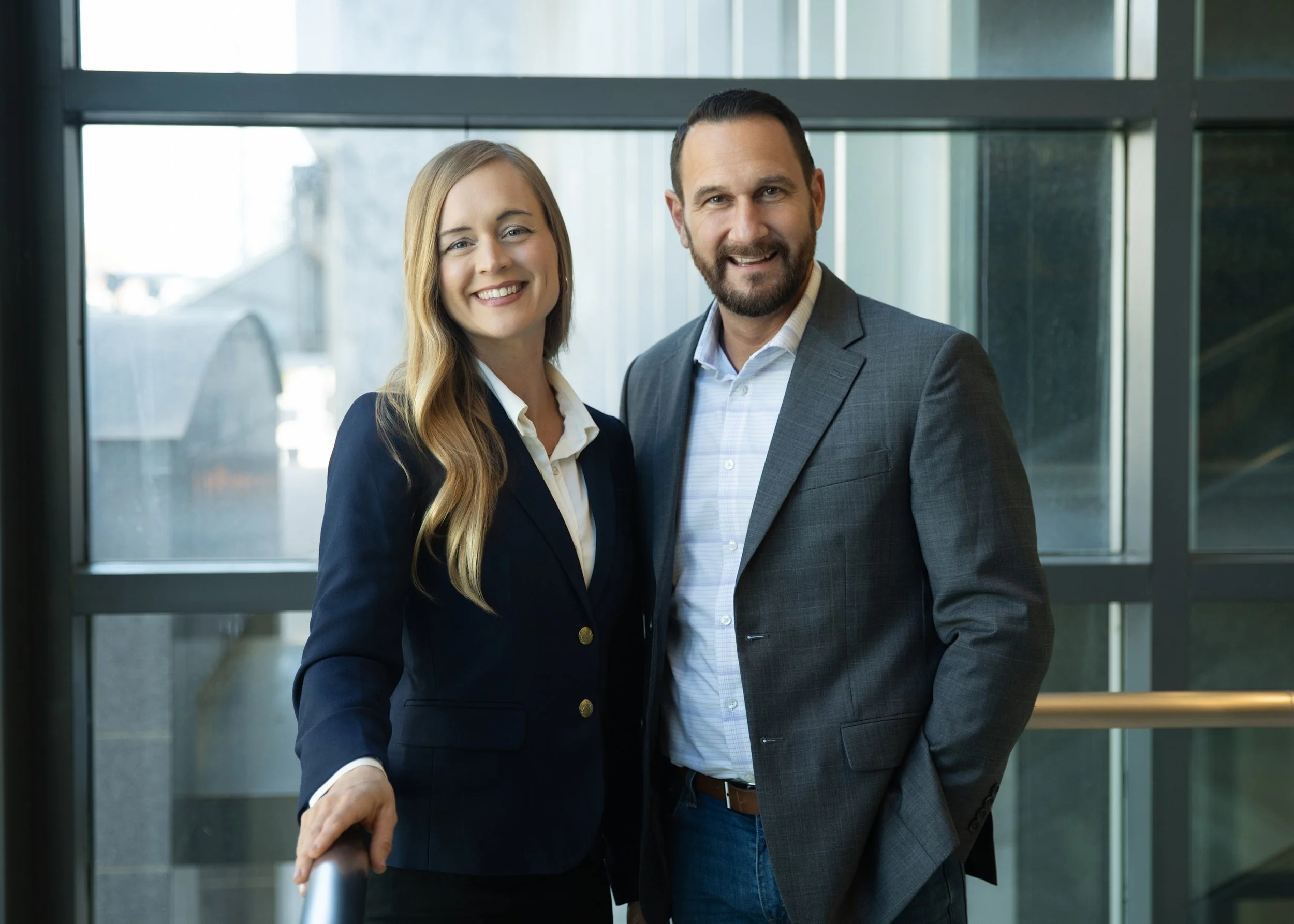 A man and woman in business attire standing infront of large window.