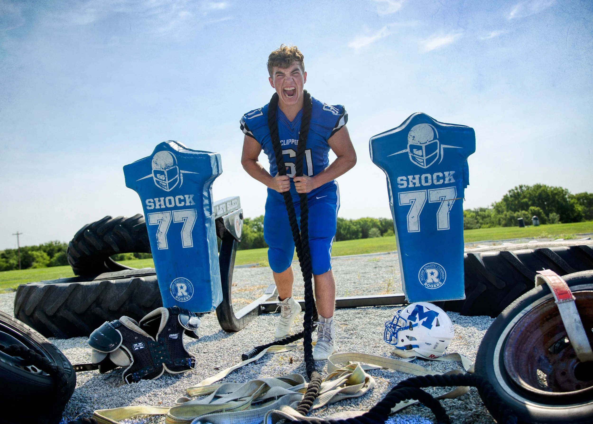 football player in his uniform with battle ropes around his neck screaming.  On each side of the athlete is blocking dummies and tires, shot by commercial photographer Corey Rourke

