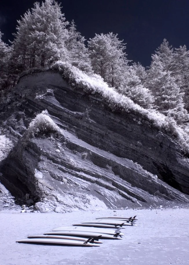 infrared image of surf boards on the beach with cliff in the background
