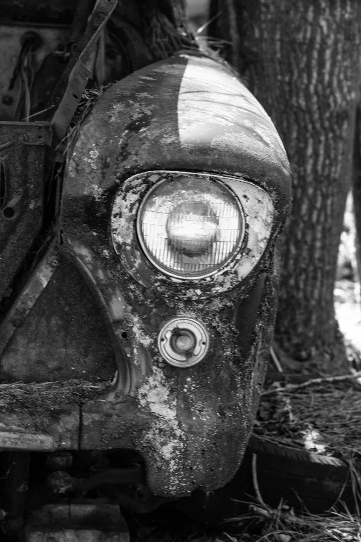 black and white image of one headlight of old abandoned car
