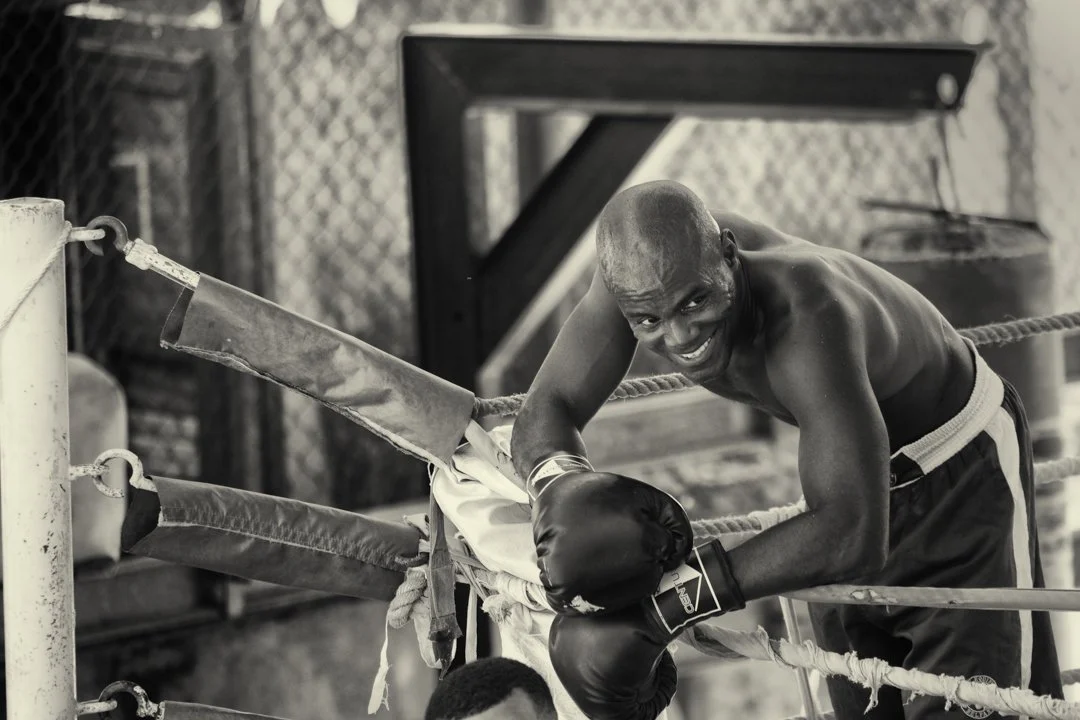 black and white image of cuban boxer smiling and leaning over rope in the ring
