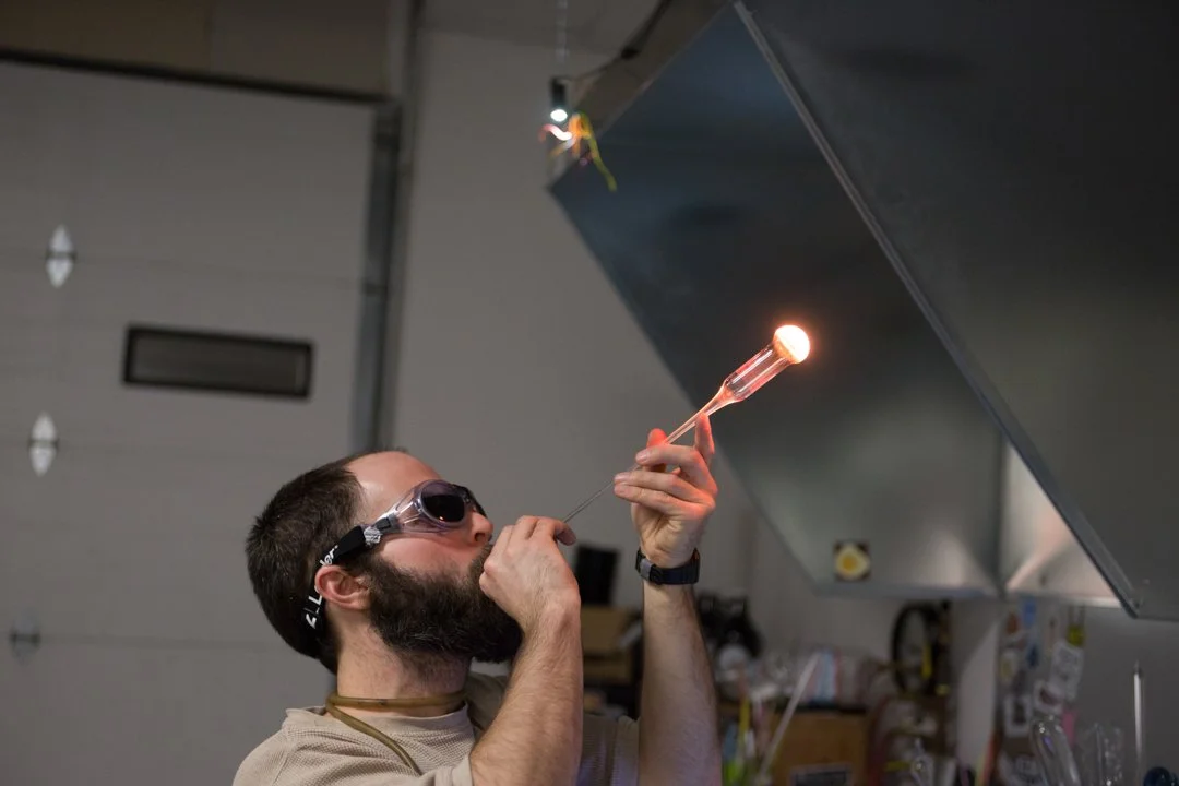 glass blower adding air to pipe to make it expand, shot by commercial photographer Corey Rourke


