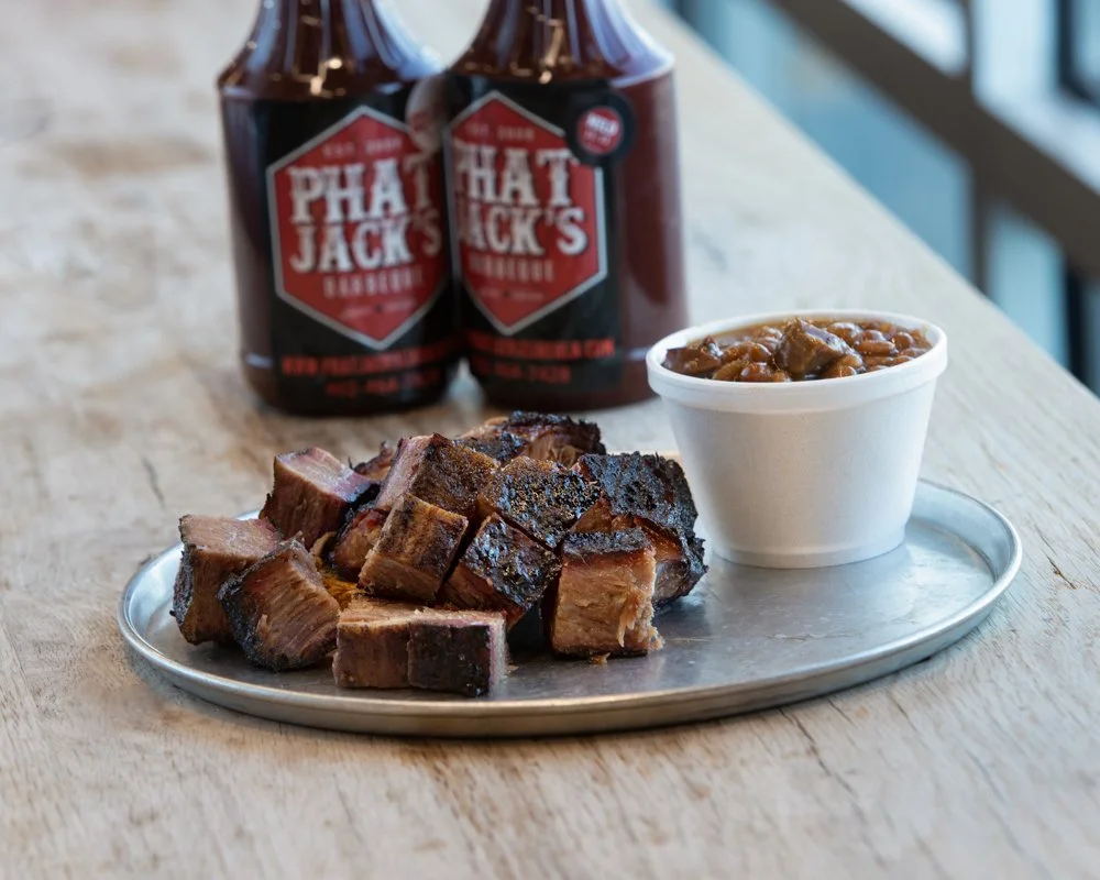 burnt ends and baked beans on silver plate with bbq sauce bottles in the background, shot by commercial photographer Corey Rourke

