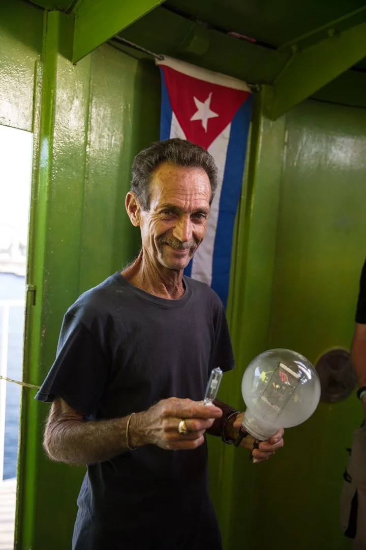 cuban lighthouse worker holding up two different size bulbs
